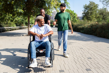 Young disabled Black man in a wheelchair and his male friends walking together in the city.