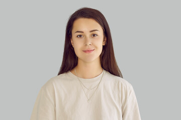 Headshot of smiling confident calm caucasian young brunette girl with long hair looking at camera. Portrait of happy cheerful millennial woman at studio isolated on grey background. People emotions.