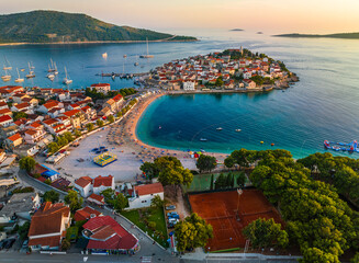 Primosten, Croatia - Aerial view of Primosten peninsula with public beach, tennis courts, St. George's Church and old town on a sunny summer afternoon in Dalmatia. Gold sky and turquoise sea water