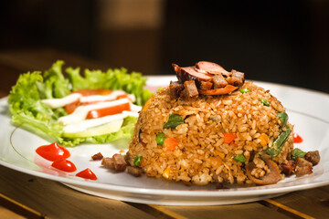 Close-up of Fried Rice  on top of white ceramic plate with salad and tomato sauce as garnish.