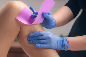 Expertise as a skilled beautician removes unwanted hair from a female leg using wax strips,...