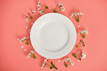White plate and branches of cherry blossoms on pink background, top view, copy space.