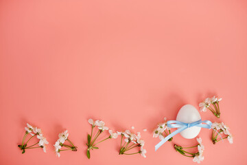 White flowers and an egg with a blue ribbon on a pink background. Easter background, a place to copy. Flat lay