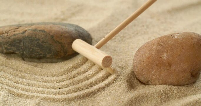 Close-up making zen garden with sand and stones using mini bamboo wooden rake