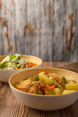 Chicken soup with vegetables in a deep bowl on a wooden table.