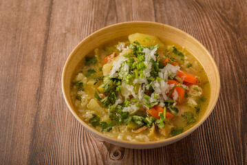 Chicken soup with vegetables in a deep bowl on a wooden table.
