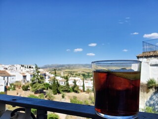 A glass of sangria ,ice black tea,or Cola,stands on the balcony railing against beautiful cityscape in Ronda,Spain