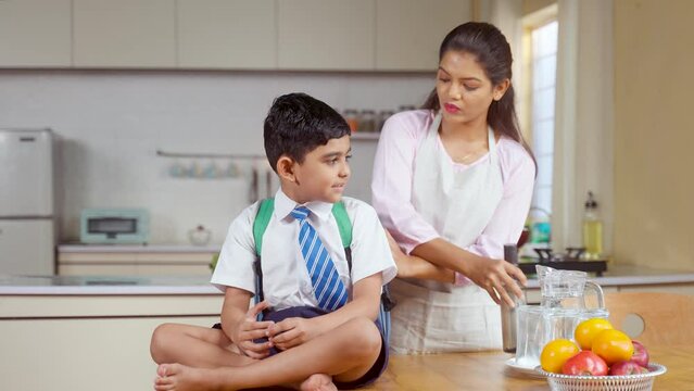 Caring Indian mother preparing kid for school by placing lunch box and water in bad - concept of responsibility, parental caring and back to school