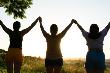 three female friends with their hands clasped high in backlight