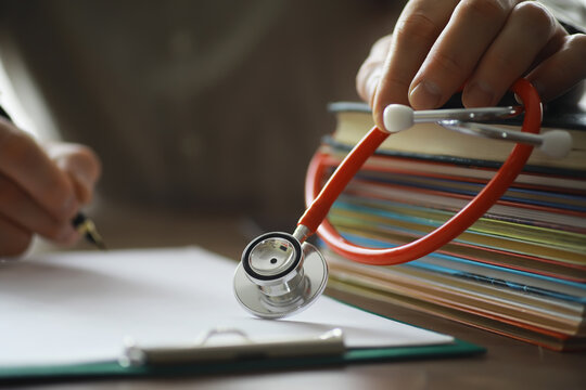 Male doctor search information in book and writtnig prescription, medical stethoscope on the desk at clinic. Medical knowledge and education concept. - Powered by Adobe