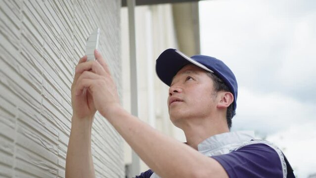 家の外壁の点検をする作業員の男性
