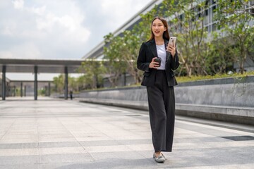 Young Asian Woman holding coffee cup and using phone outdoor in a central business district area