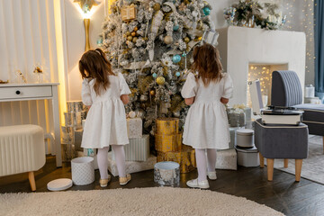 Two twin sisters in a white dress decorate the Christmas tree with their own hands, Christmas holidays at home.