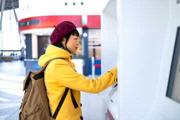 Female passenger with backpack buying train ticket at self-service machine.