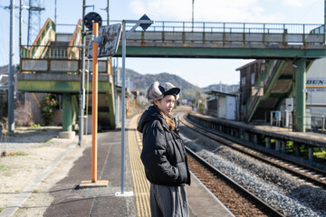 田舎の駅のホームで電車を待つ女性