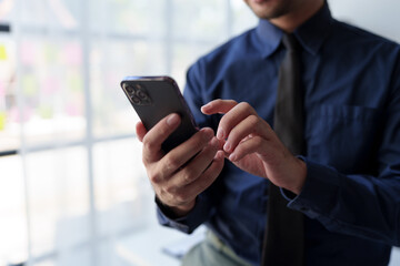 Businessman relaxes holding smartphone, checking email, work details on laptop computer online, contacting, business negotiation with customer pointing to successful business goals in office.