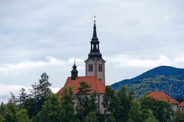 Lake Bled with church on an island and woodland in the background on a cloudy summer day. Photo taken August 8th, 2023, Bled, Slovenia.