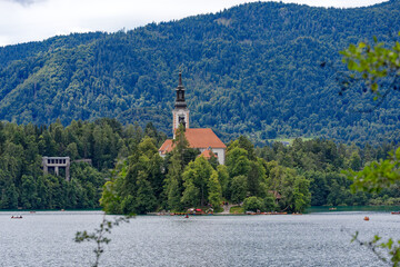 Fototapeta na wymiar Lake Bled with church on an island and woodland in the background on a cloudy summer day. Photo taken August 8th, 2023, Bled, Slovenia.