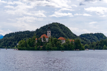 Fototapeta na wymiar Slovenian Lake Bled with church on an island and mountain panorama with woodland in the background on a cloudy summer day. Photo taken August 8th, 2023, Bled, Slovenia.