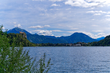 Slovenian Lake Bled with church on an island and mountain panorama with woodland in the background on a cloudy summer day. Photo taken August 8th, 2023, Bled, Slovenia.