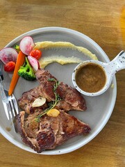 Pork steak with vegetables and sauce on the white dish on wooden table