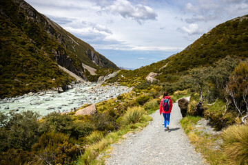 Fototapeta premium hiker girl walking alongside hooker valley track toward hooker lake and mt cook, famous walk in canterbury, new zealand south island