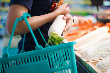 Woman holding grocery basket walk in supermarket. Attractive. female hold radish, pick up from...