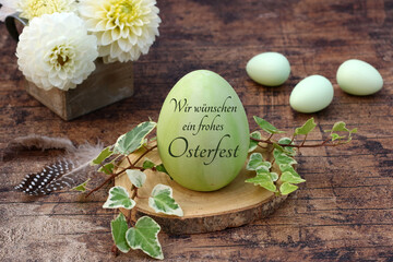 Frohe Ostern: Blumenstrauß mit Ostereiern auf einer Baumscheibe dekoriert. Beschriftetes Osterei...