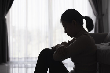 Silhouette of a person suffering from depression in the house, Depressed woman sitting alone on the Sofa feel stress, sad and worried in the dark room. person are stressed.