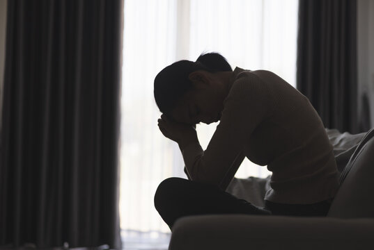 Silhouette of a person suffering from depression in the house, Depressed woman sitting alone on the Sofa feel stress, sad and worried in the dark room. person are stressed.