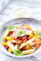 Penne pasta with yellow and red pepper, hard cheese and fresh basil. Bright background. Close up.	