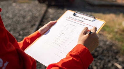 	
Action of a mechanic engineer is checking on heavy machine checklist form to verify the quality of maintenance service, with train locomotive part as blurred background. Industrial working scene.