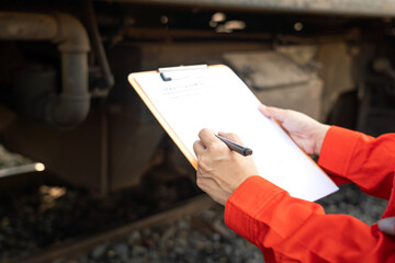 	
Action of a mechanic engineer is checking on heavy machine checklist form to verify the quality of maintenance service, with train locomotive part as blurred background. Industrial working scene. - obrazy, fototapety, plakaty
