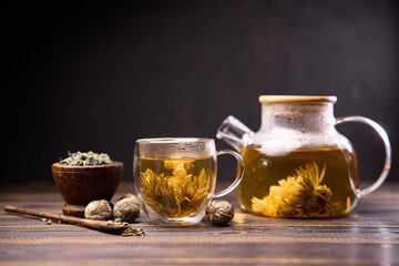 Teapot and glass cup with blooming tea flower inside on a wooden table