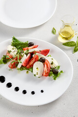 Classic Caprese salad with ripe tomatoes, mozzarella, and olives, garnished with fresh basil. Suitable for Italian cuisine promotions and cookbooks