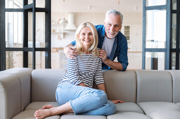 Middle age man cuddling from back his wife, couple looking at camera