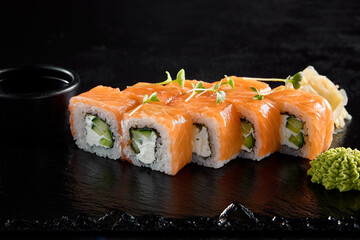 Philadelphia roll with salmon on a black slate, accompanied by soy sauce and wasabi
