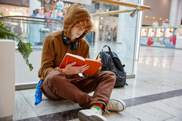 Teenage boy writing in notebook while sitting on floor of shopping mall