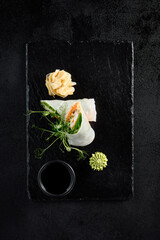 Top view of a shrimp spring roll with green pea sprouts on a black slate