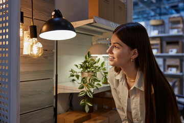 Young pretty woman choosing lamp for her apartment at store