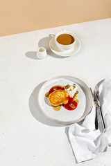 Pancakes topped with cream cheese, berry sauce, and mango, accompanied by coffee with milk