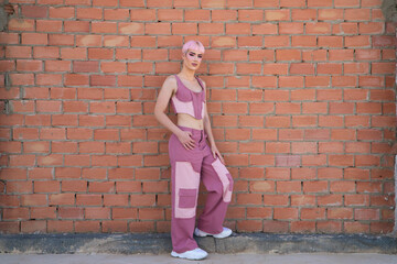 Young gay boy with pink hair and make-up leaning against a brick wall. The boy is dressed modernly in shades of pink. Concept of equality and LGBTQ rights.