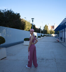 Young gay guy with pink hair and makeup walks down the street and poses for the photo. The boy is dressed in pink with modern clothes. Concept of equality and LGBTQ rights.