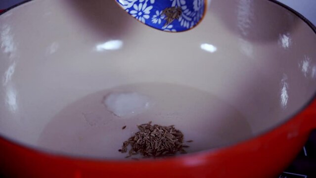 Adding some cumin seeds to a pot of coconut oil to make fresh green papaya curry