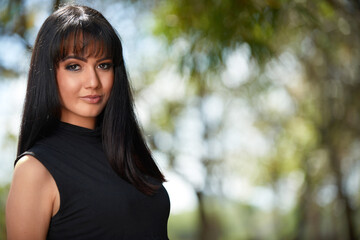 Naklejka premium Confident young woman in urban park wears trendy jeans, a belly-revealing black top, exuding casual elegance and style