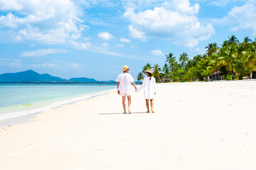 a couple of men and woman with summer hats walking at the beach of Koh Muk