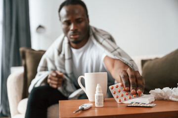 Obraz na płótnie Canvas Holding pills that are on the table. Sick black man is at home