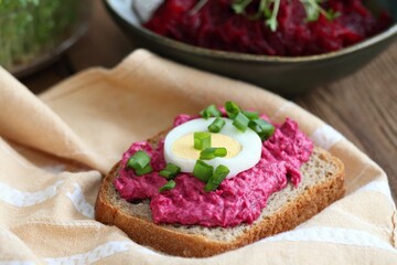 Beetroot mixed with goat cream cheese spreaded on whole grain bread. Spread decorated with slice of an egg and green onion, beetroot salad and herbs at back.