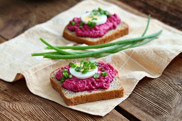 Fototapeta na wymiar Beetroot mixed with goat cream cheese spreaded on whole grain bread. Spread decorated with slice of an egg and green onion.