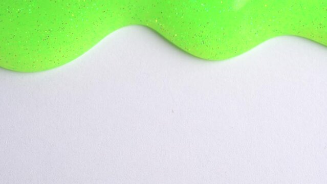 Green neon glitter sparkle confetti background liquid drops of paint color flow down on white canvas. Light green glitter paint dripping on the craft paper wall and filling the screen.